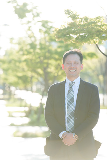 光を背に笑顔で立つ小林